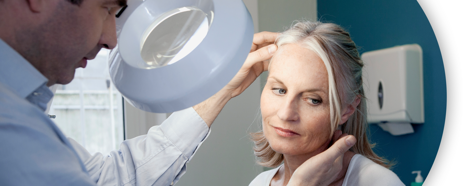 Male physician examining an older woman's face through a magnifier