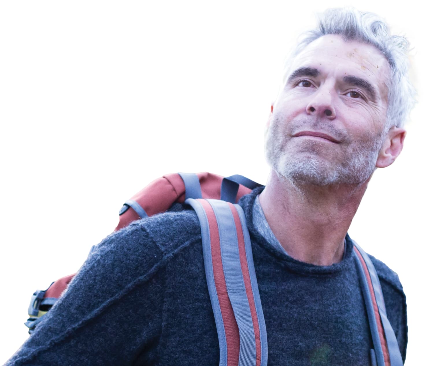 A man with gray hair wearing a dark sweater and a backpack looks upward with a calm expression, suggesting he is outdoors or hiking.